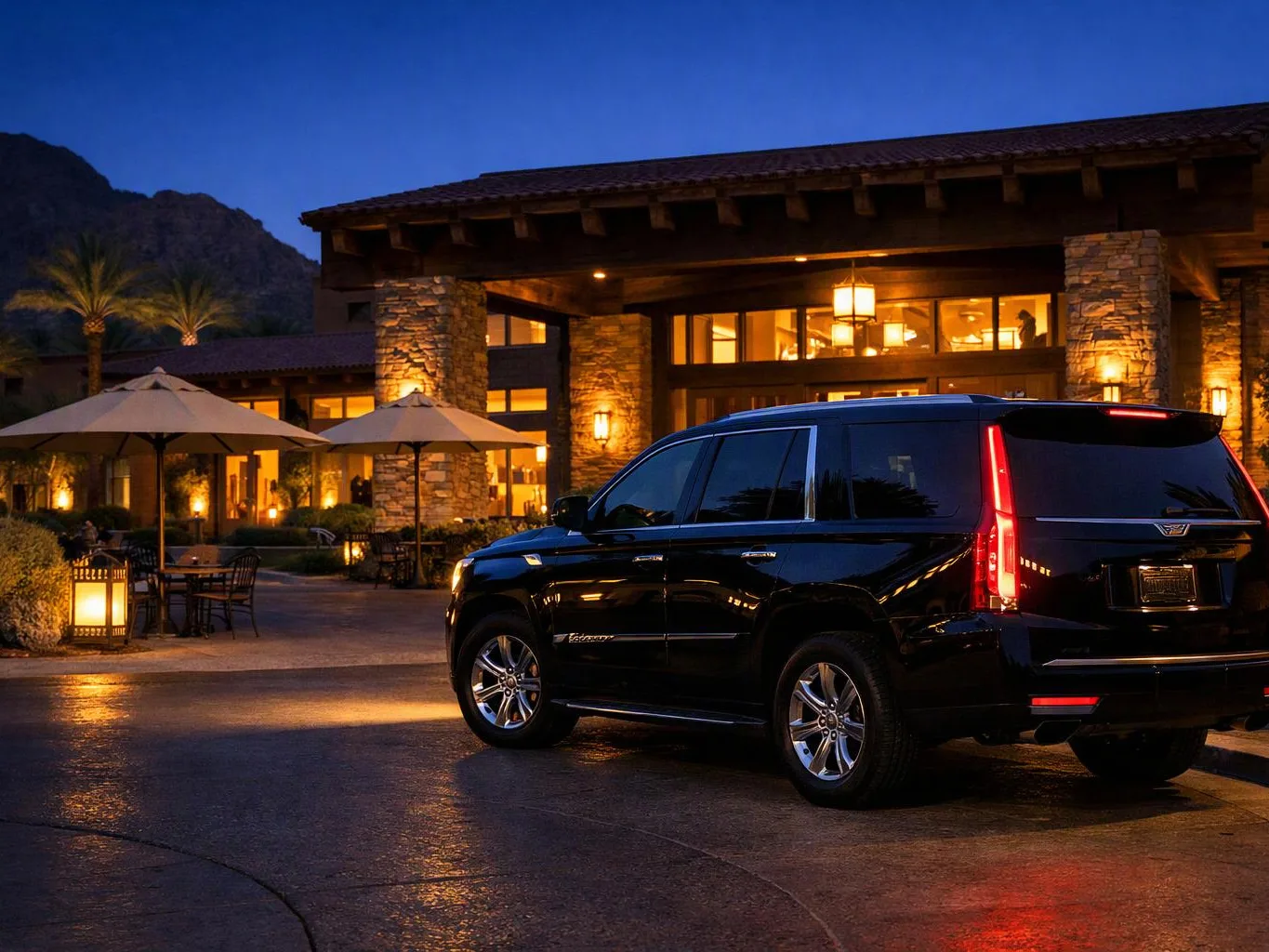 A black SUV is parked outside a warmly lit stone lodge at dusk, with mountains in the background