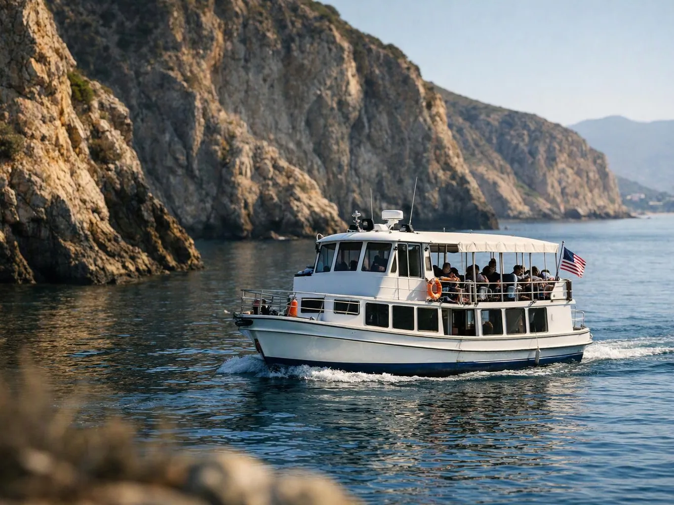 A white passenger boat cruises past steep rocky cliffs on calm blue water