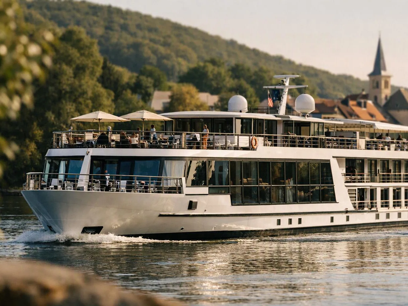 A white river cruise ship glides past green hills, with passengers on the sunlit upper deck